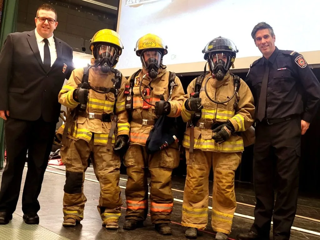 Deux hommes en uniformes encadrent 3 jeunes portant l'équipement de pompier