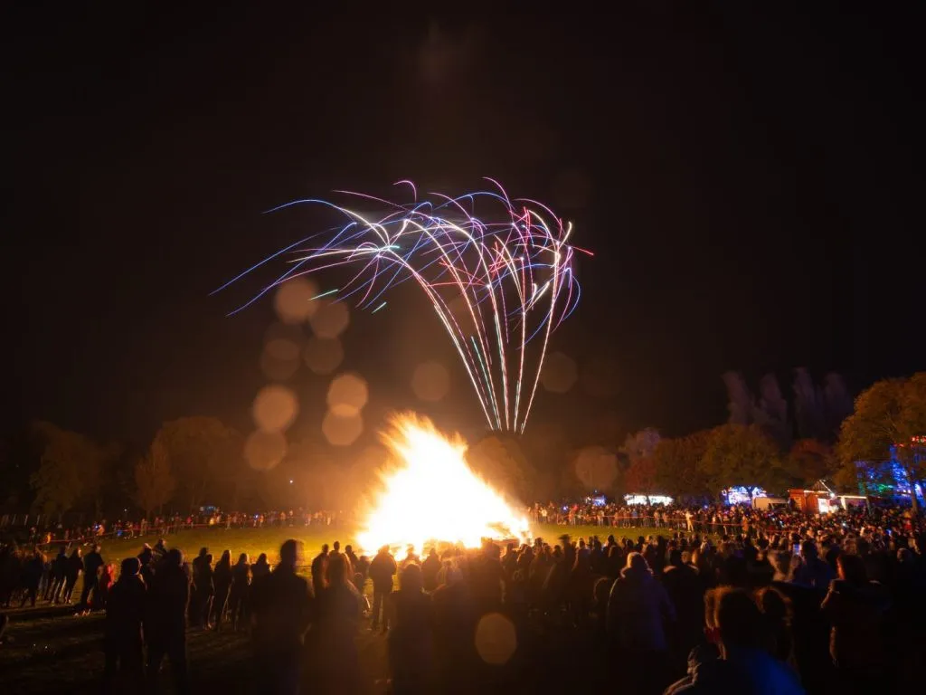 Un grand feu avec des centaines de personnes autour et des feux dartifices. 