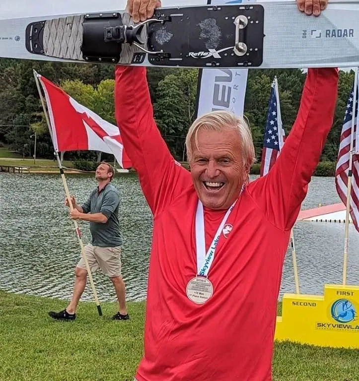 Un homme âgé les bras en l'air avec un médaille autour du cou.