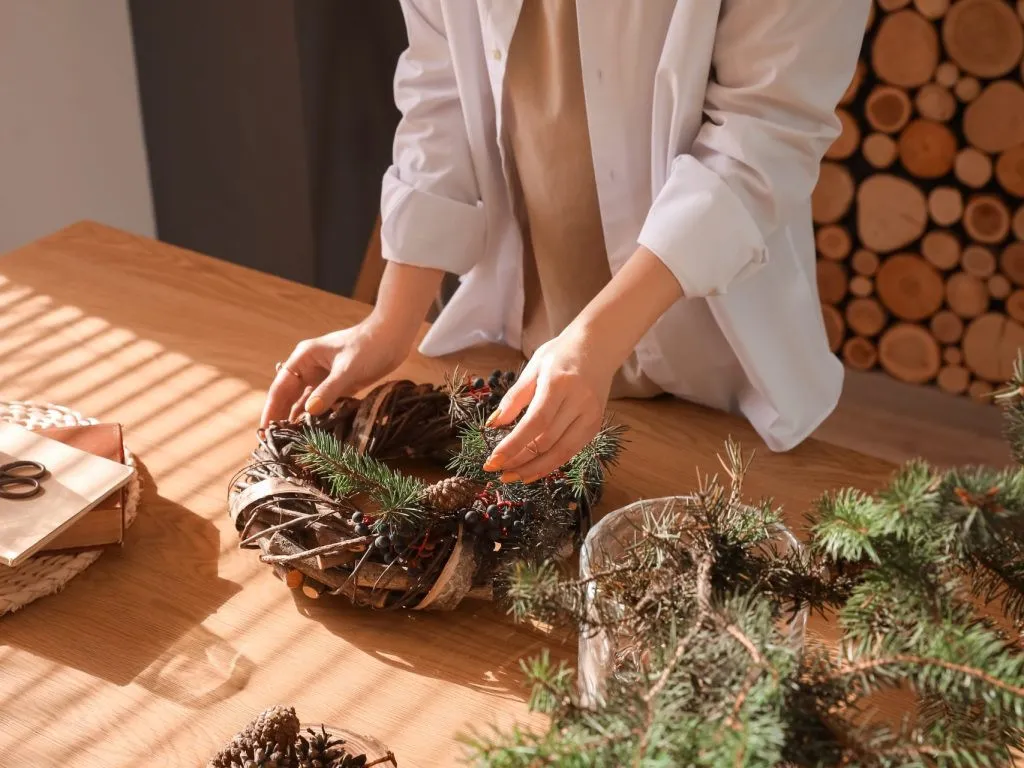 Une femme qui assemble une couronne de Noël pour l'installer comme centre de table