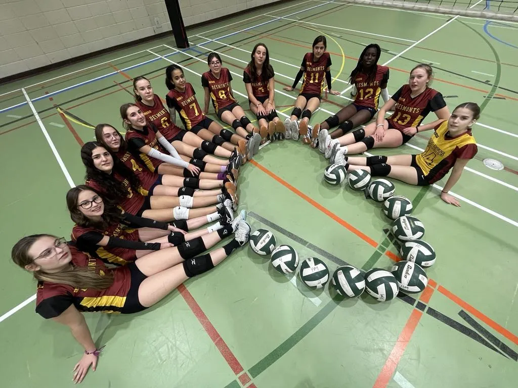 Des filles assises au sol forment un coeur avec leur peid et des ballons de volleyball